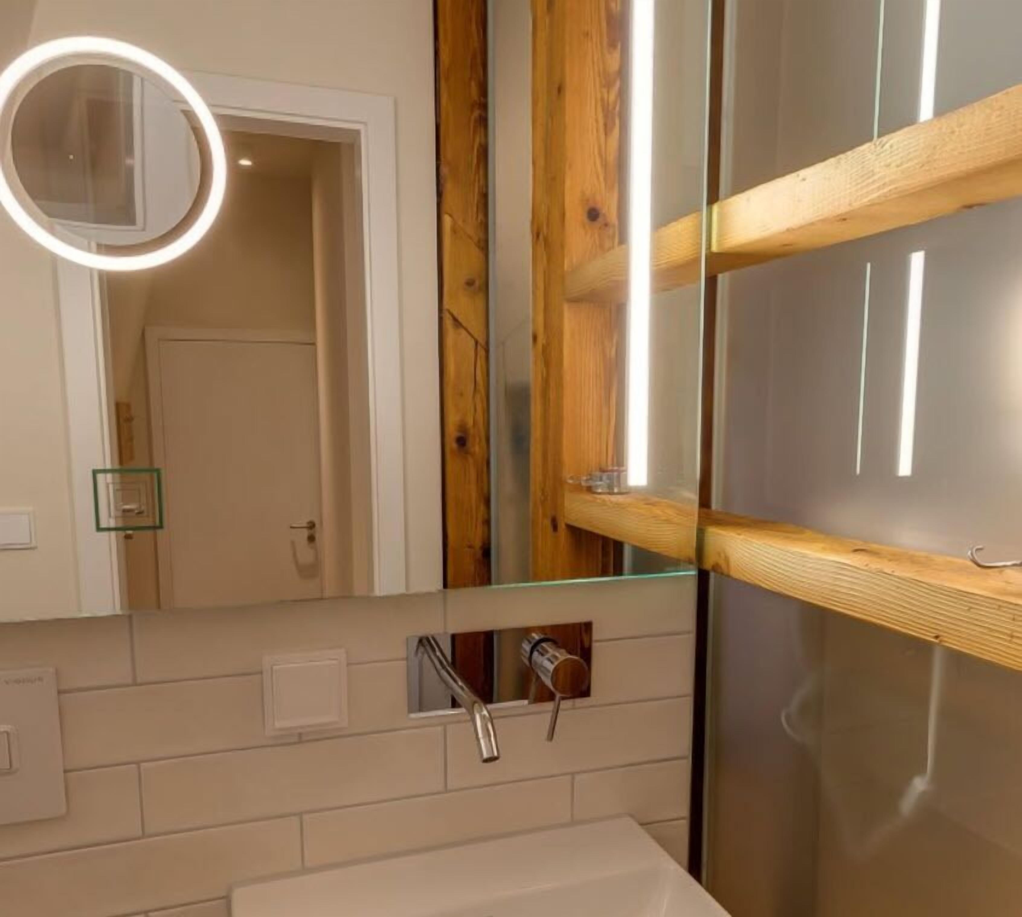 A bathroom with a wooden beam structure, a glass shelf, a round mirror with a light, and a white sink.