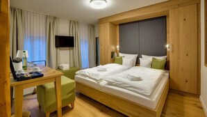 Habitación de hotel con una cama de madera, un escritorio con lámpara, televisión y una ventana con cortinas.