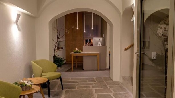 Un interior moderno con suelo de piedra, zona de comedor con mesa y sillas, y cocina al fondo.
