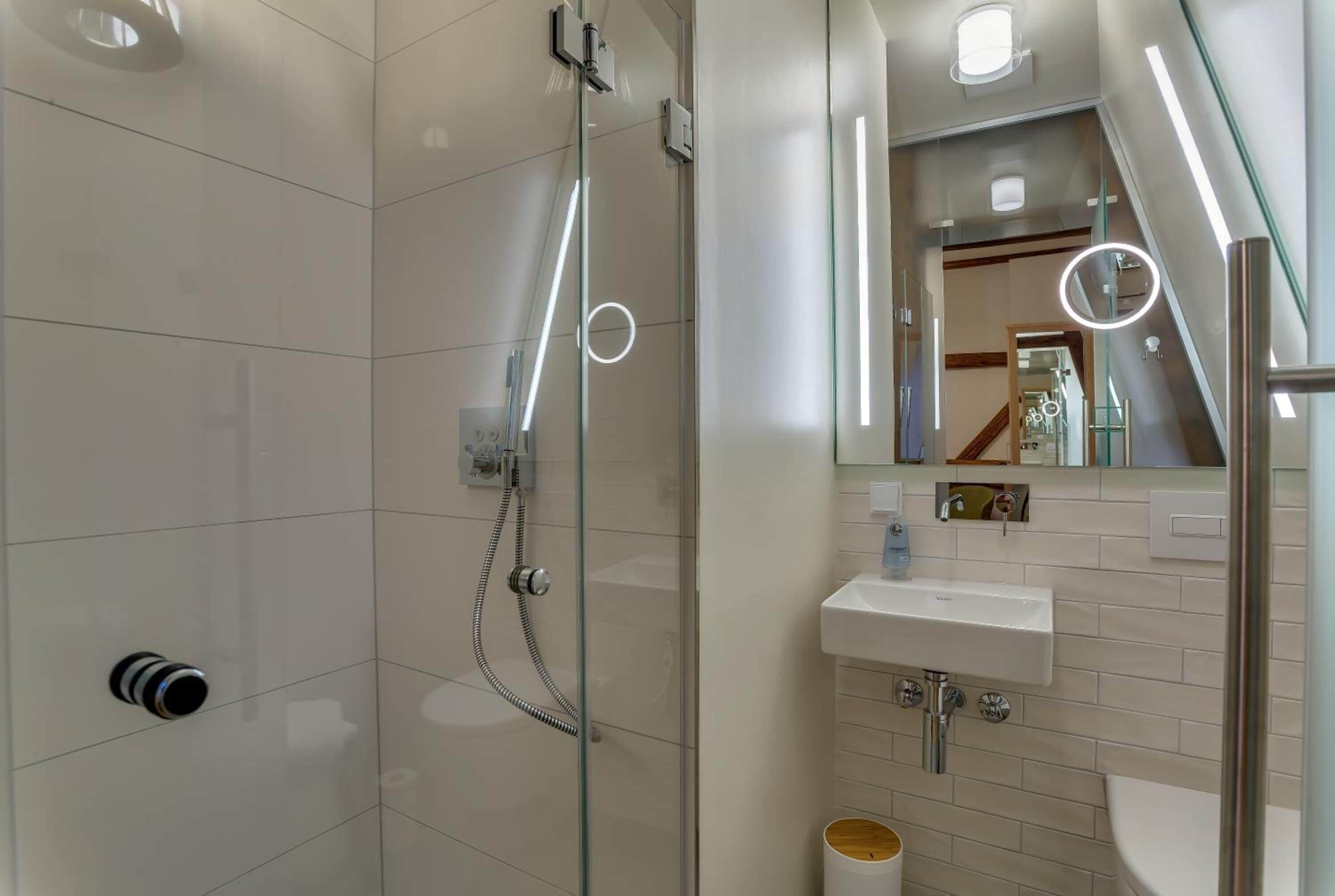 Een moderne badkamer met een douchecabine van glas, een wastafel en een spiegel met ingebouwde verlichting.