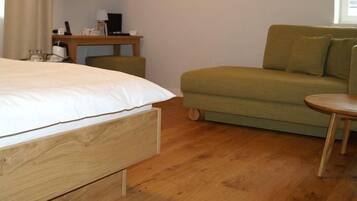 A bedroom with a bed, a green sofa, a small table, and a wooden nightstand with a lamp and a phone.