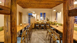 Un comedor rústico con mesas y sillas de madera, un alto techo de madera y ventanas arqueadas.