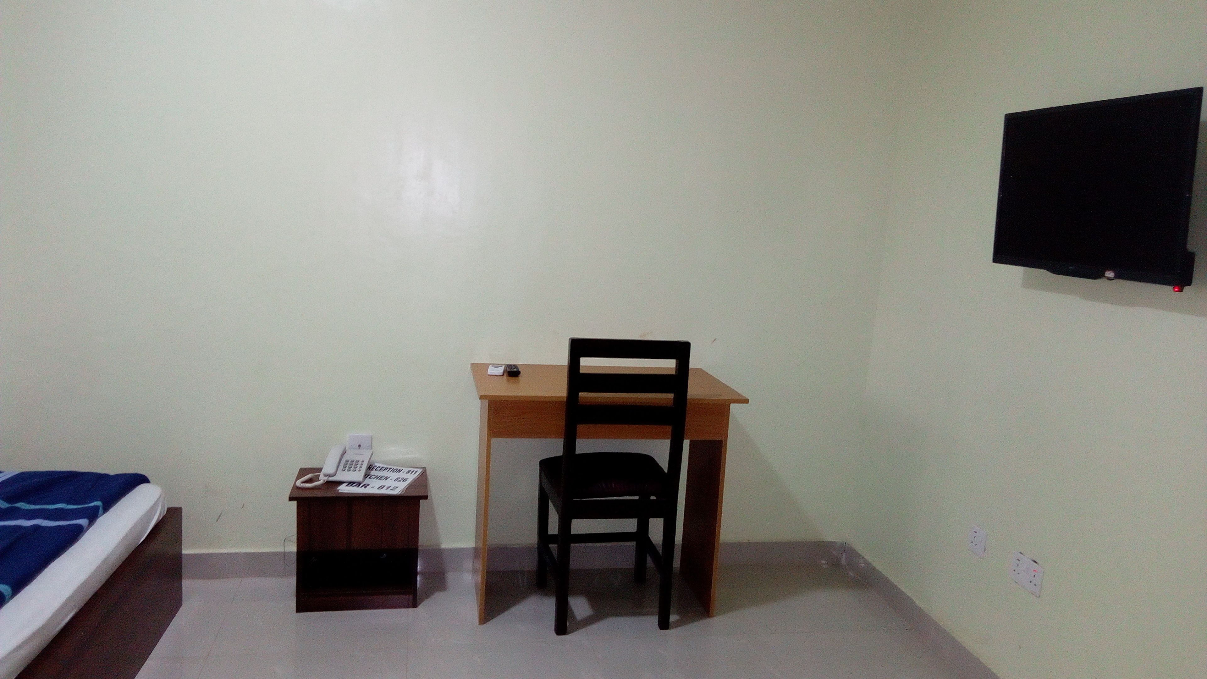 Une petite pièce comprenant un lit, un bureau avec une chaise, un téléphone et un téléviseur fixé au mur.