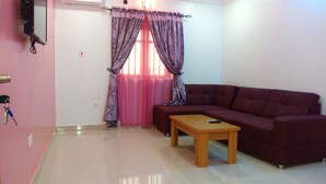 A living room with a sofa, a wooden coffee table, and a TV mounted on the wall. - Denposon Royal Hotel (Lagos)