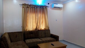 A living room with a sofa, a coffee table, and an air conditioning unit on the wall. - Denposon Royal Hotel (Lagos)