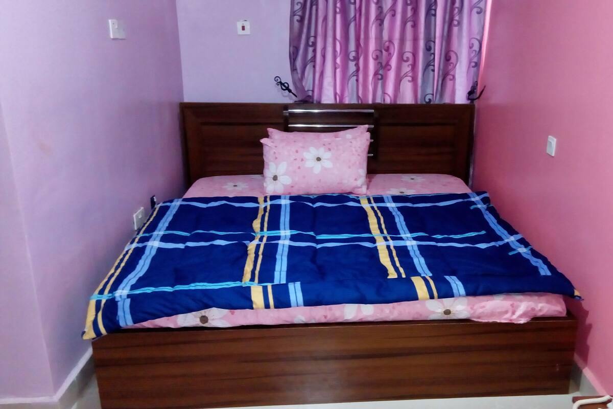 A single bed with a wooden frame, a blue and yellow striped bedspread, and a pink pillow with a floral pattern.