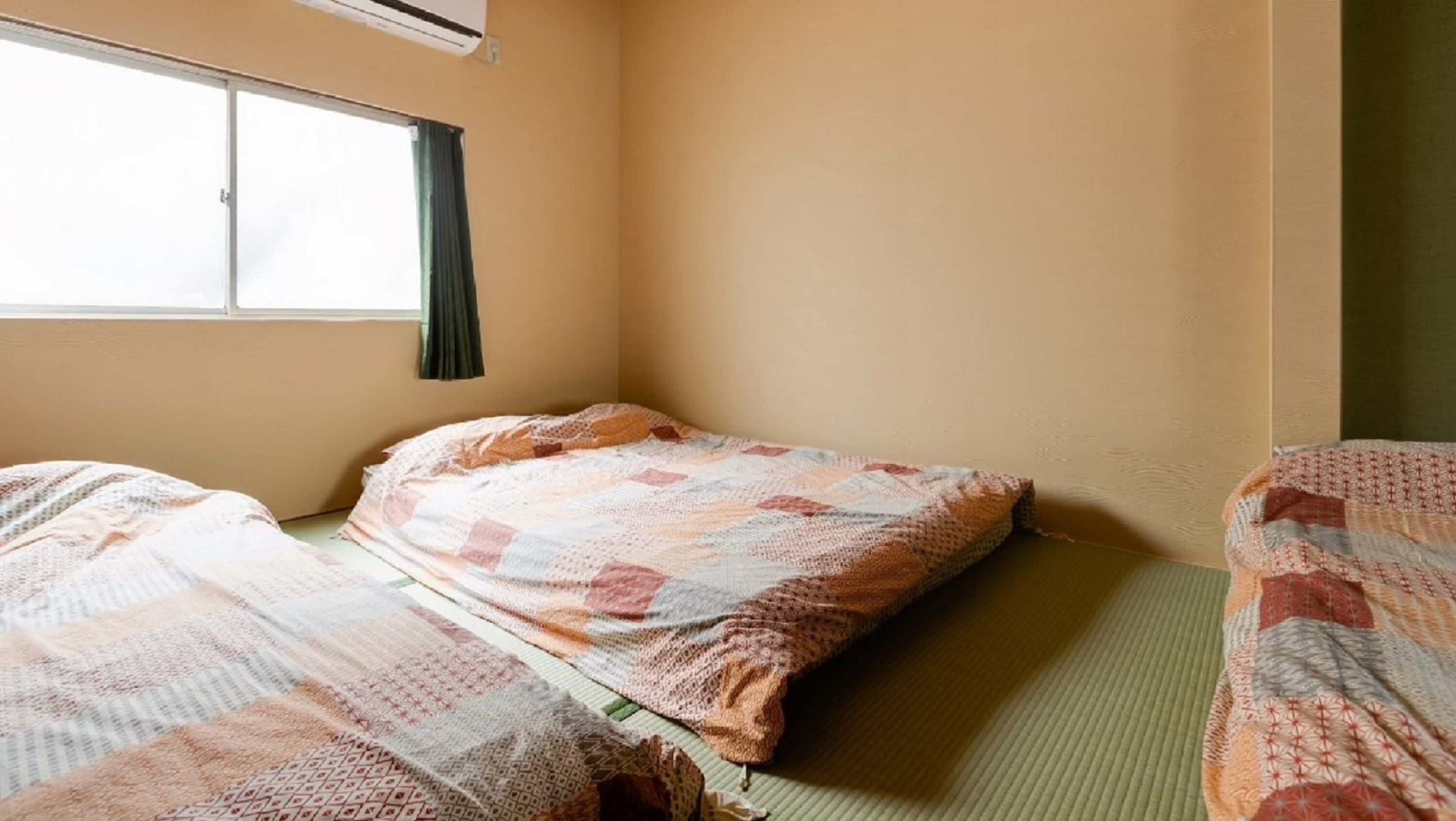 A small, single-bed room with a window, a green curtain, and a bedspread.
