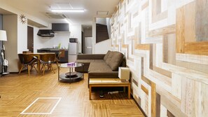 Un espacio habitable compacto con sofá, una mesita, una silla y zona de cocina.