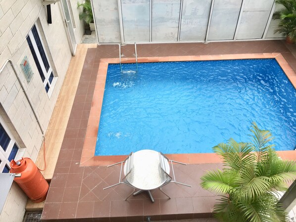 A rectangular swimming pool with a metal ladder, surrounded by tiled flooring and a metal table with chairs.