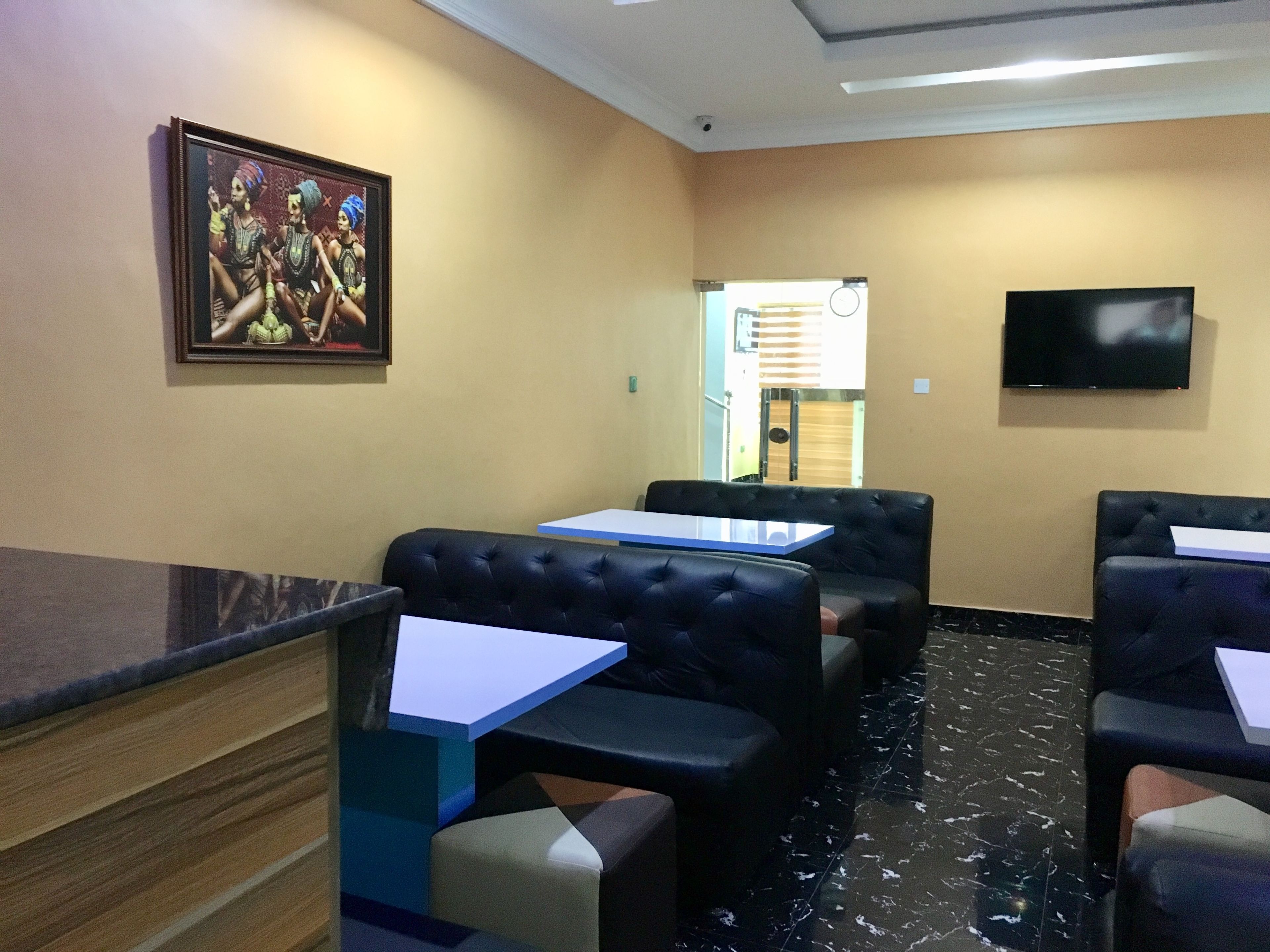 A hotel lobby with a reception desk, seating area with cushioned chairs, a television mounted on the wall, and a framed picture on the wall.