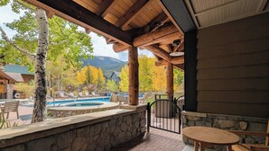 A covered outdoor area with a pool, stone walls, wooden furniture, and a view of a mountain and autumn trees. - Summer Base | Patio, Pool & Hot Tub (keystone)