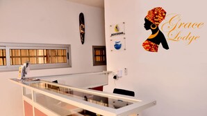 Un mostrador de recepción con una mampara de vidrio, un letrero en la pared con logotipos y la silueta de una mujer con el texto "Grace Lodge".