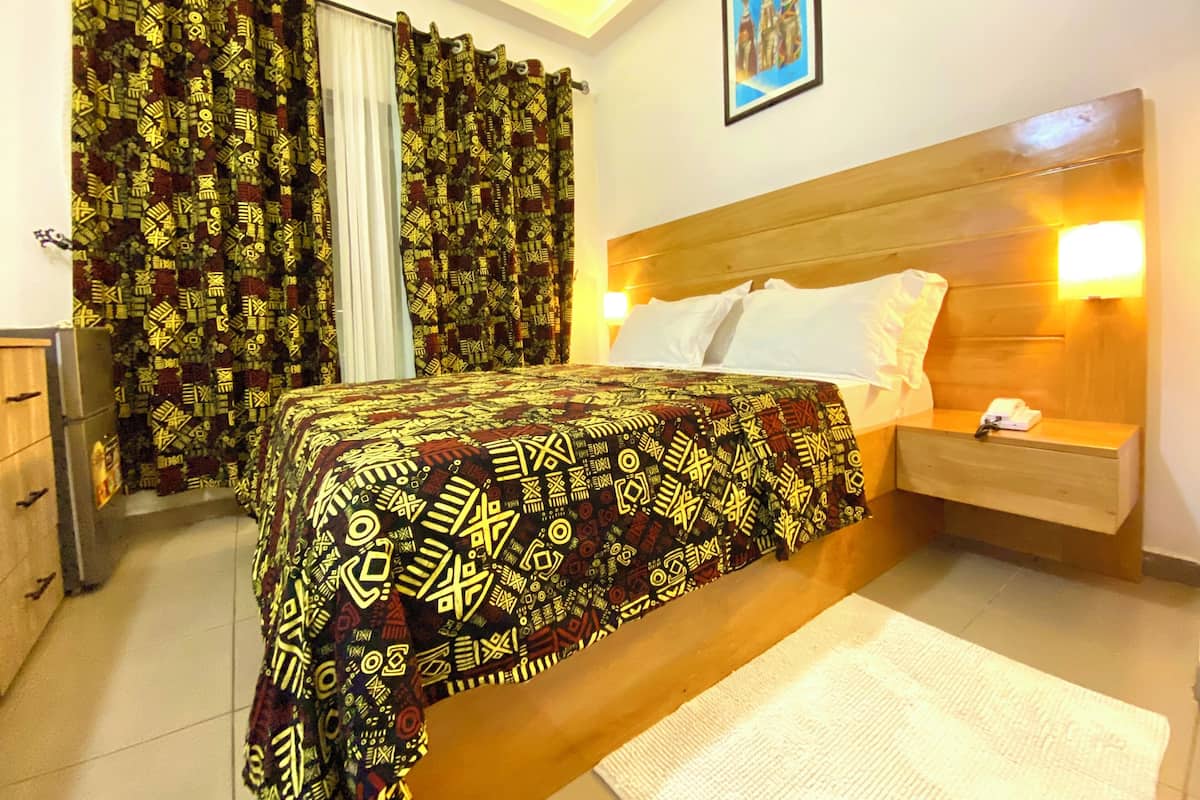 Una habitación de hotel con cama, mesita de noche, lámpara, armario y cortinas estampadas.