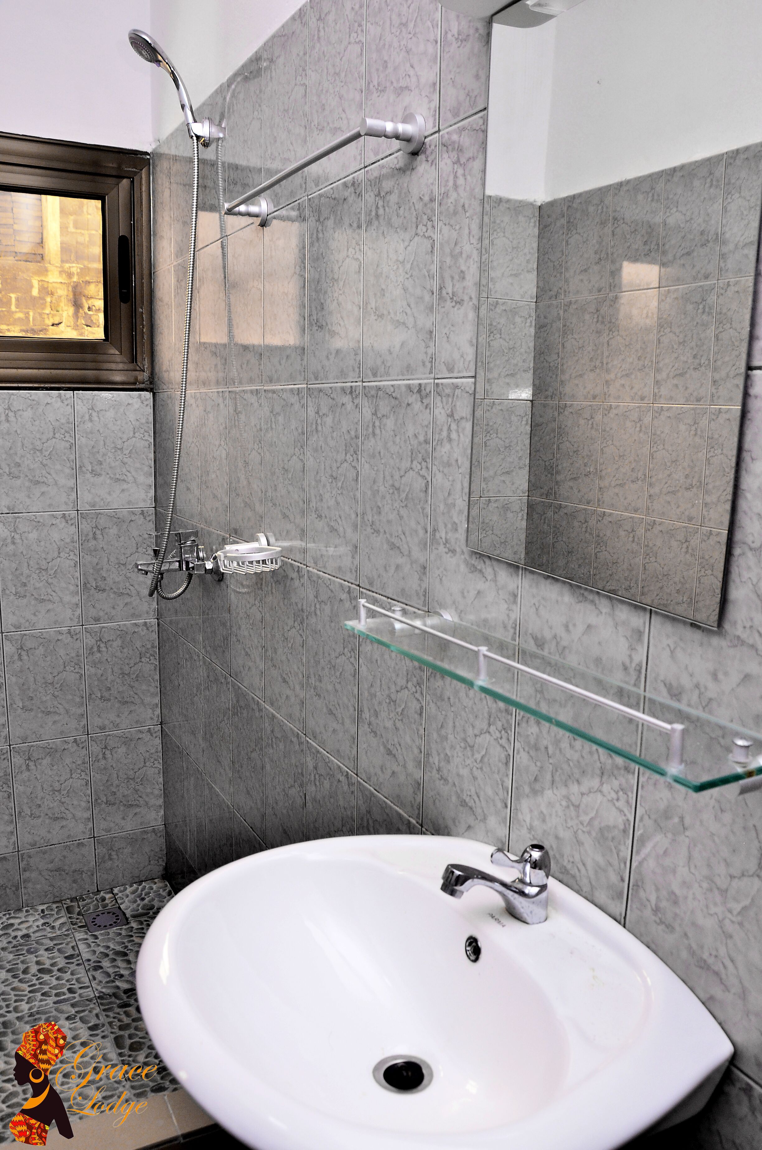 A bathroom with a white sink, a glass shelf, a shower with a handheld showerhead, and a mirror on the wall.
