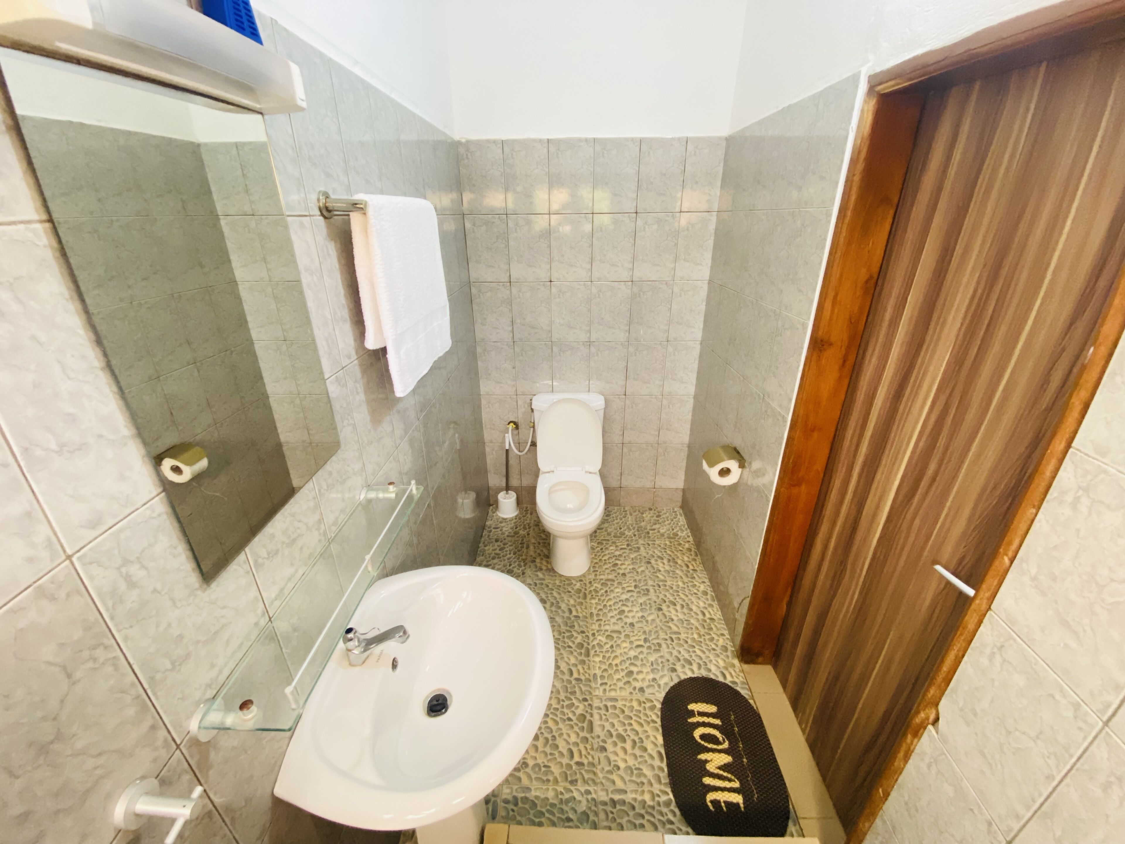 A bathroom with a white sink, toilet, and a mirror. There is a towel hanging on the wall and a door with a wooden frame.