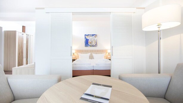 A hotel room with a bed, a desk, a chair, a lamp, and a painting on the wall.