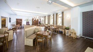 A spacious hotel lobby with wooden flooring, multiple seating areas, and large windows allowing natural light.