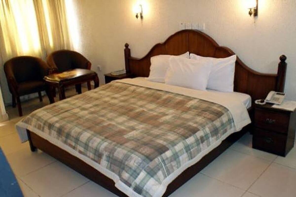 A hotel room with a bed, two chairs, a nightstand, and a lamp.