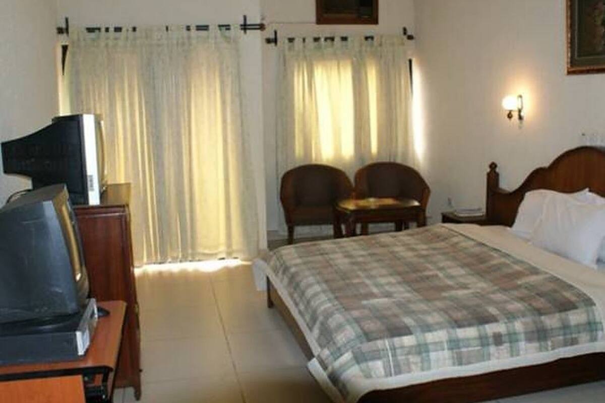 A hotel room with a bed, two chairs, a desk with a television, and curtains.