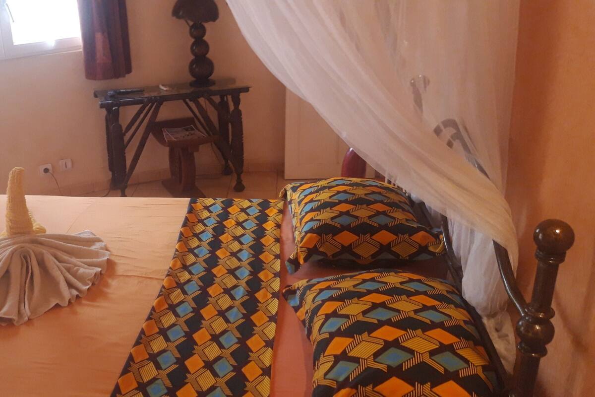 A bed with a patterned bedspread, a bedside table, a lamp, and a window with curtains.