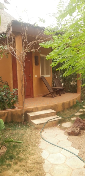 Una casa con puerta roja, un porche pequeño y un jardín con manguera.