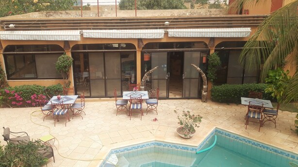 A building with a pool area, outdoor seating, and a covered patio. - Auberge Le Dakan (Mbour)