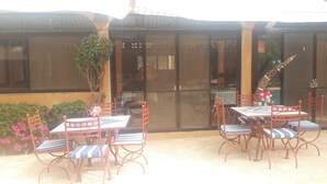 An outdoor patio with a table and chairs, a glass door, and a view of the interior. - Auberge Le Dakan (Mbour)