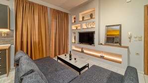A modern living room with a sofa set, a flat-screen TV, built-in shelves, and a small dining table. - Amoudara Suites (Malevizi)