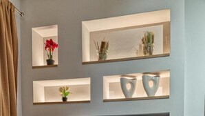 A modern living room with a flat-screen TV mounted on a wall, surrounded by shelves with decorative items and a wine bottle on a coffee table. - Amoudara Suites (Malevizi)
