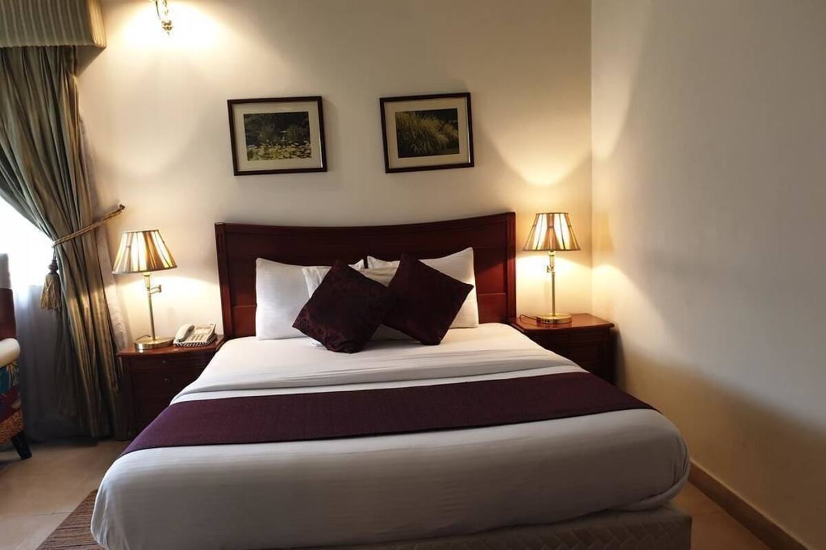 Une chambre d’hôtel avec un grand lit, deux lampes de chevet, un téléphone et deux tableaux encadrés au mur.