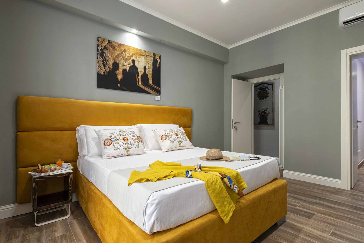 A bedroom with a large bed, a bedside table with a tray of breakfast, and a painting on the wall.
