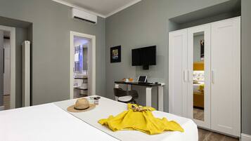 Ein Hotelzimmer mit Bett, Flachbildfernseher an der Wand, Kleiderschrank und Schreibtisch mit Stuhl.