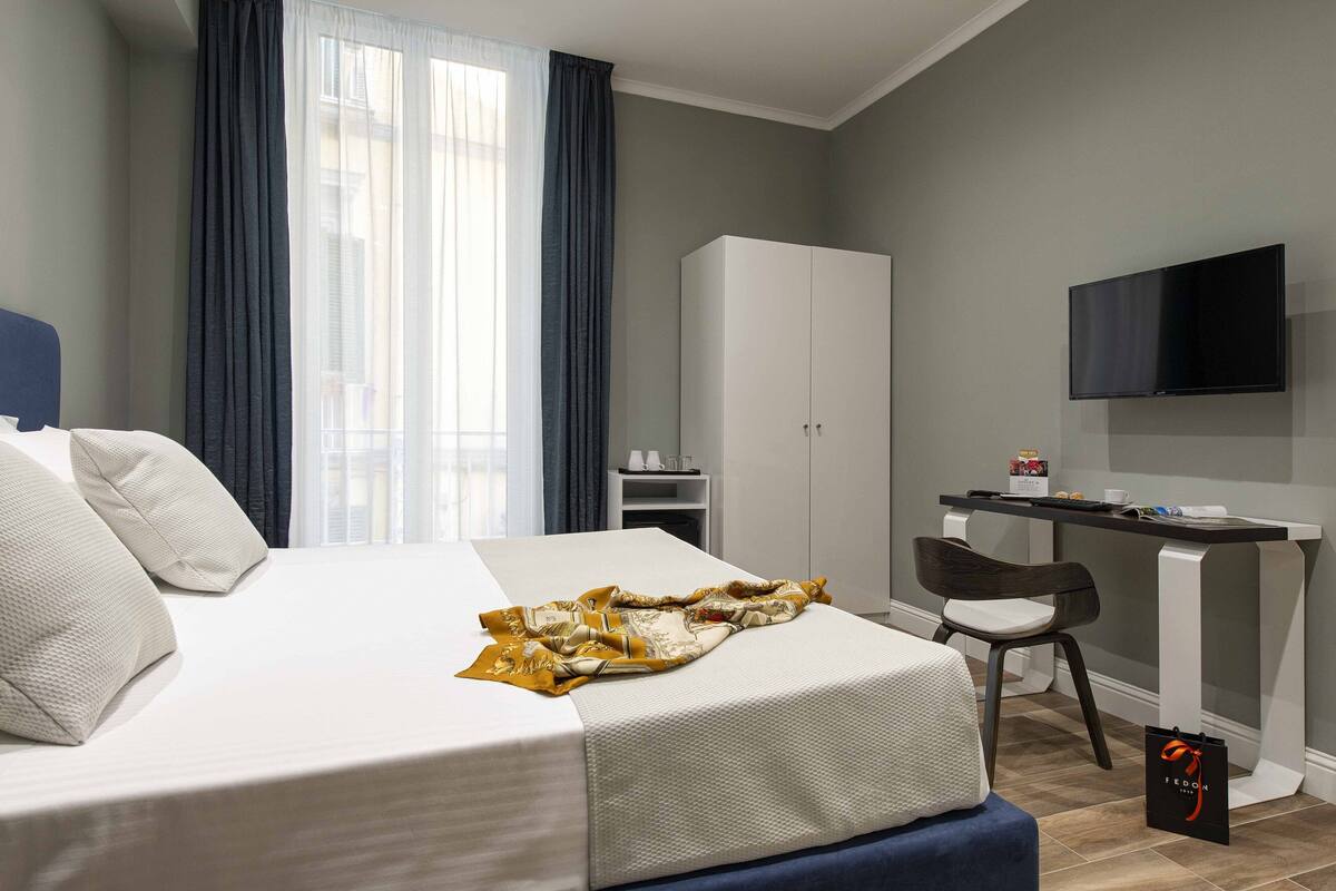 A hotel room with a bed, a desk, a chair, a wardrobe, and a TV.