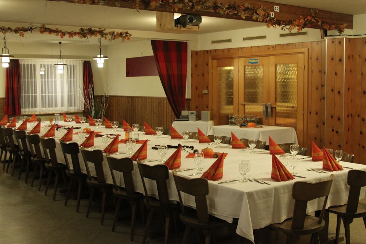 A long dining table with multiple chairs, set with white tablecloths and orange napkins.