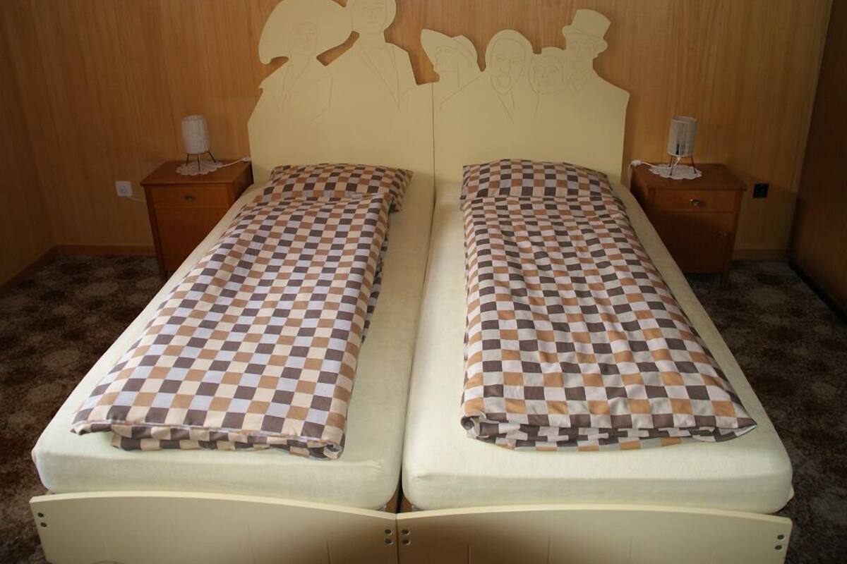 A double bed with a checkered bedspread, two bedside tables with lamps, and a wooden headboard with cut-out designs.