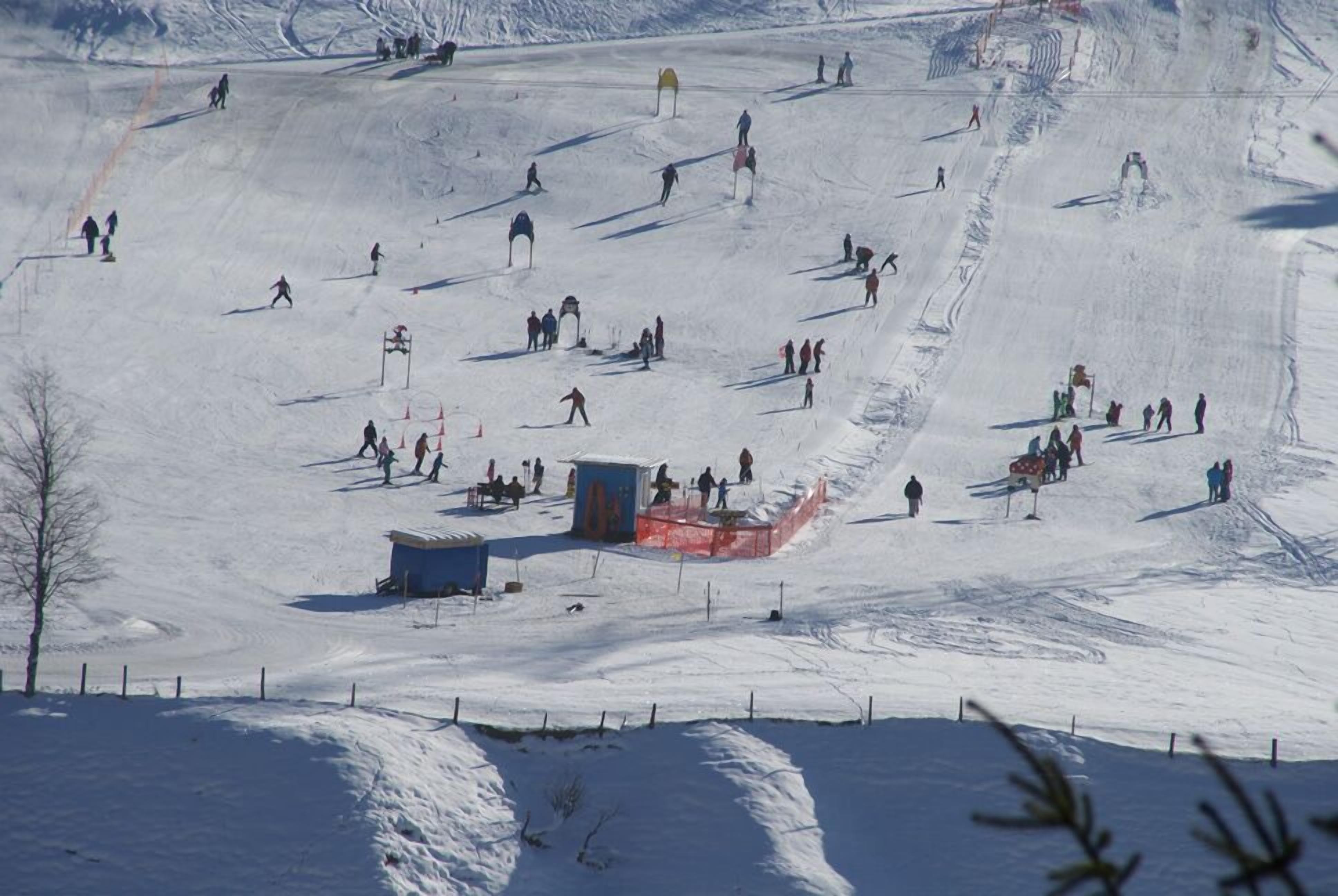 A ski slope with skiers and snowboarders, a small shelter, and a fenced area.