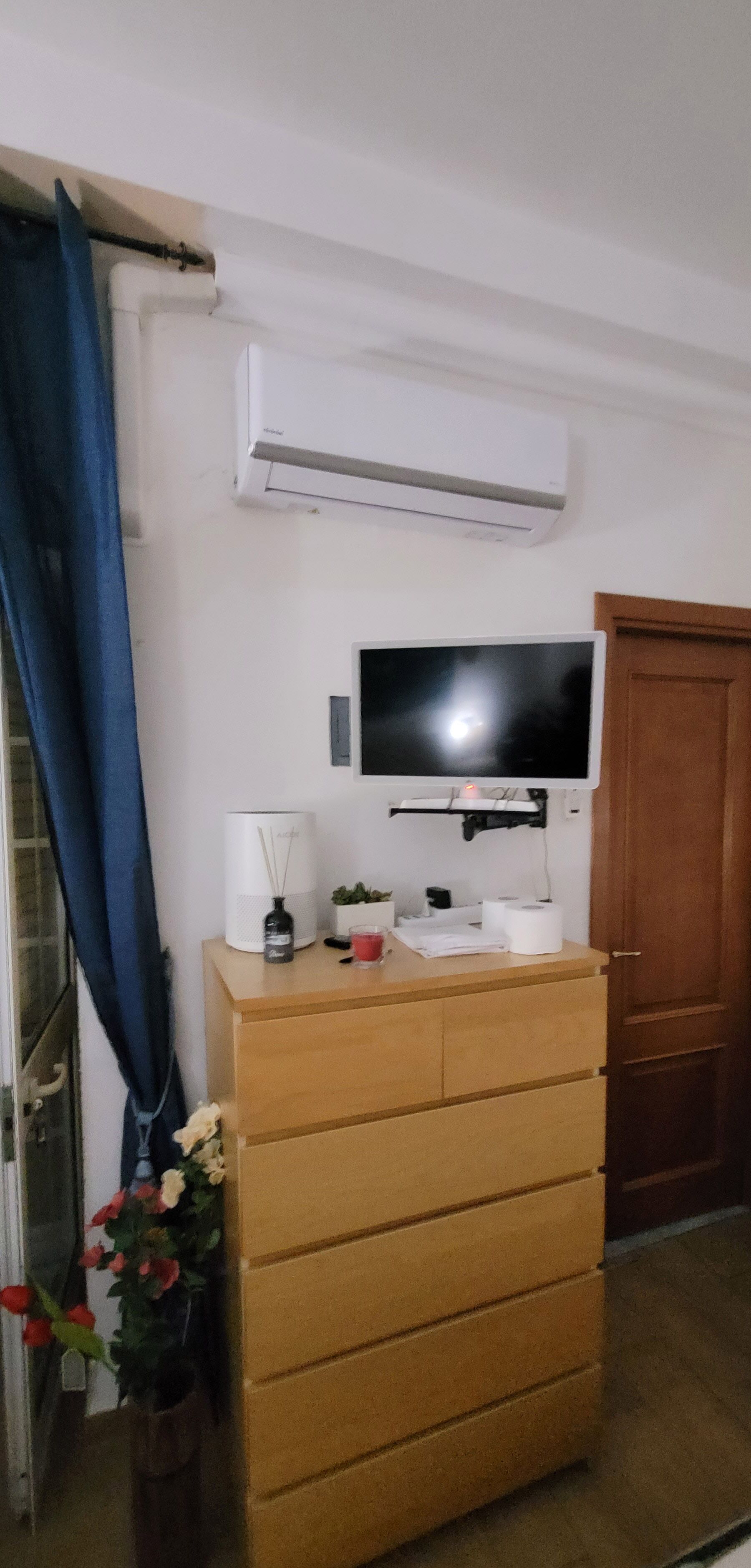 Una habitación con un aparador de madera, un televisor de pantalla plana, aire acondicionado, una cortina azul y una puerta de madera.