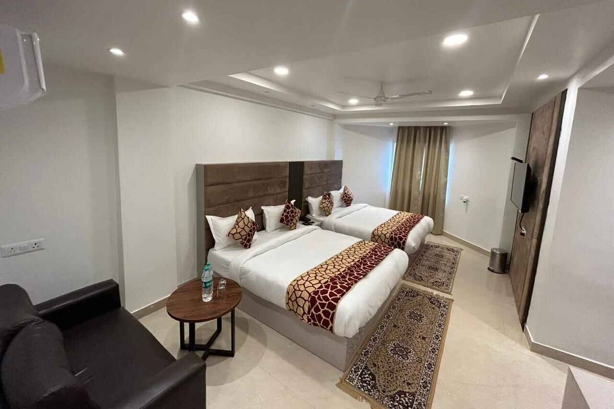 A hotel room with two beds, a small table, a sofa, and a TV.