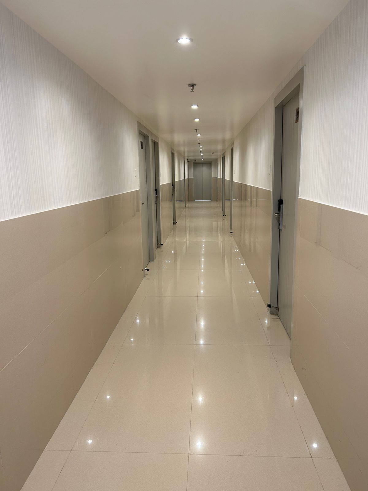 A long, well-lit corridor with doors on both sides, leading to a central elevator area.