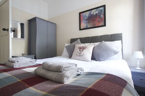 A neatly made bed with a plaid bedspread, a grey headboard, and several pillows, including one with a floral design. - Handbridge House (Chester)