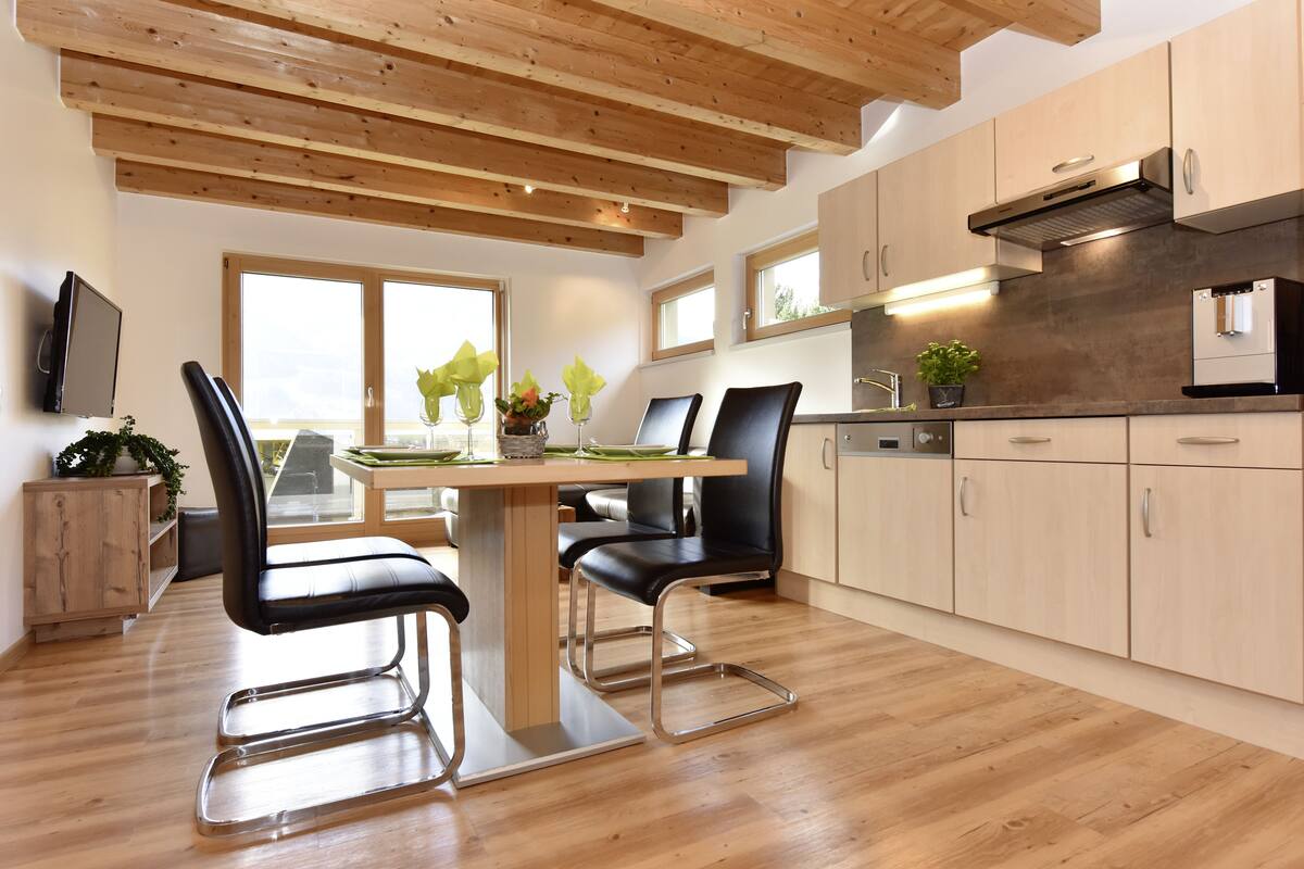 A modern kitchen with wooden beams, a dining area with a table and chairs, and a built-in oven.