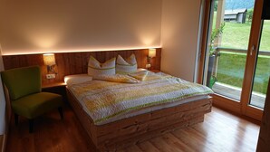 Un dormitorio con estructura de cama de madera, una silla verde y una mesita de noche con una lámpara.