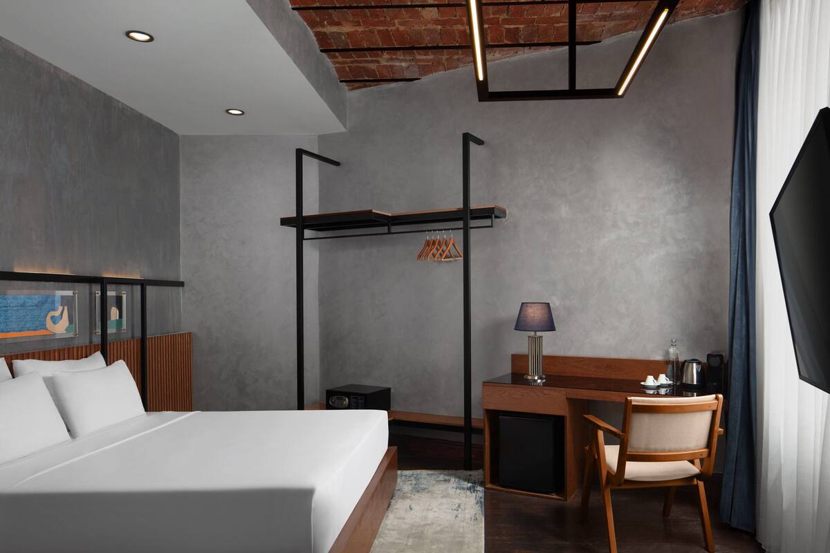 A modern hotel room with a bed, desk, chair, and a hanging coat rack.