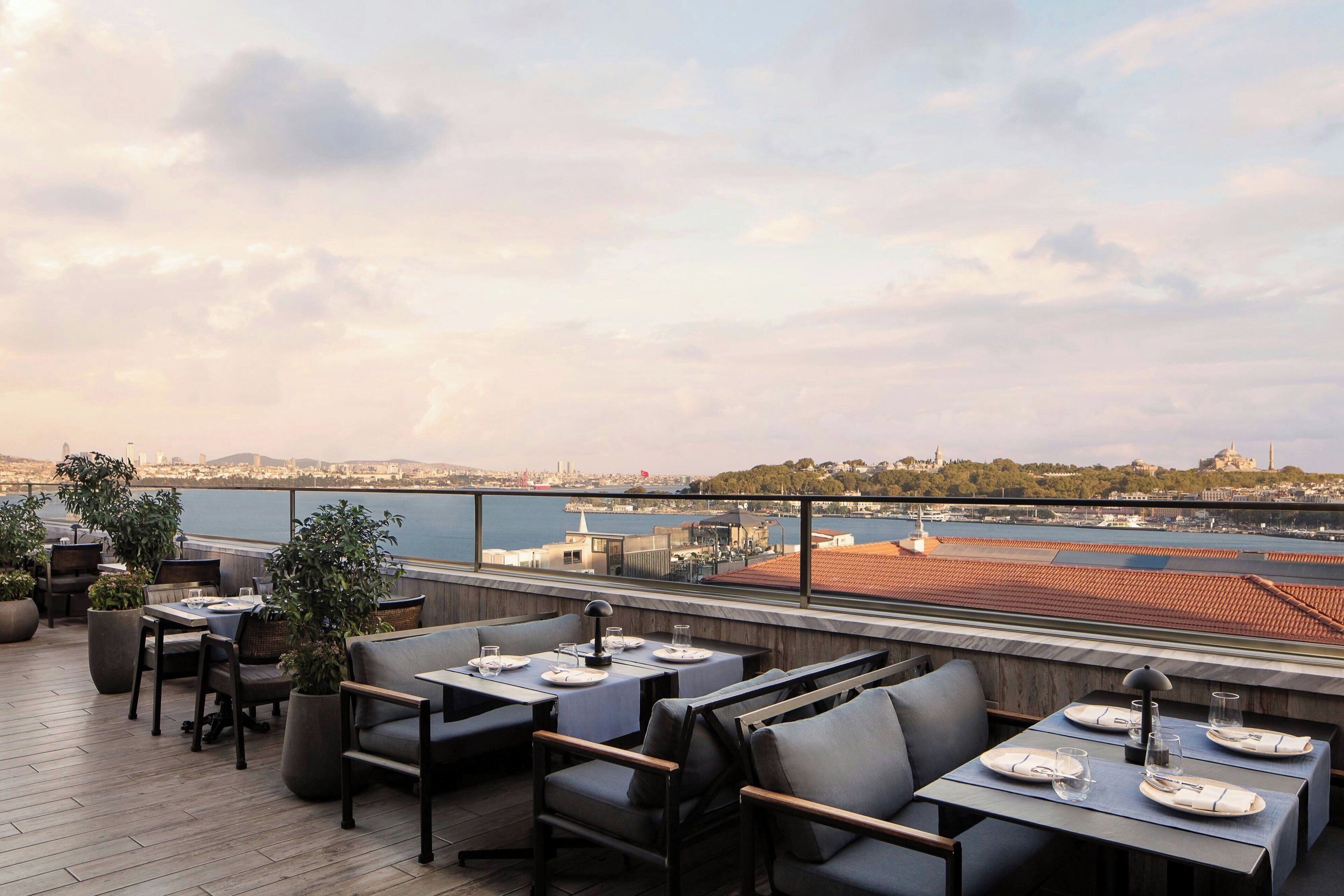 An outdoor dining area with tables and chairs, overlooking a waterfront cityscape.