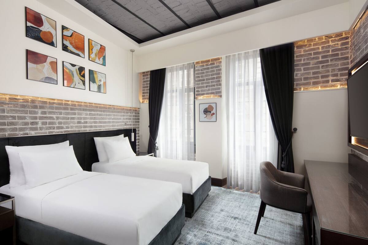 A hotel room with two beds, a desk, a TV, and artwork on the walls.