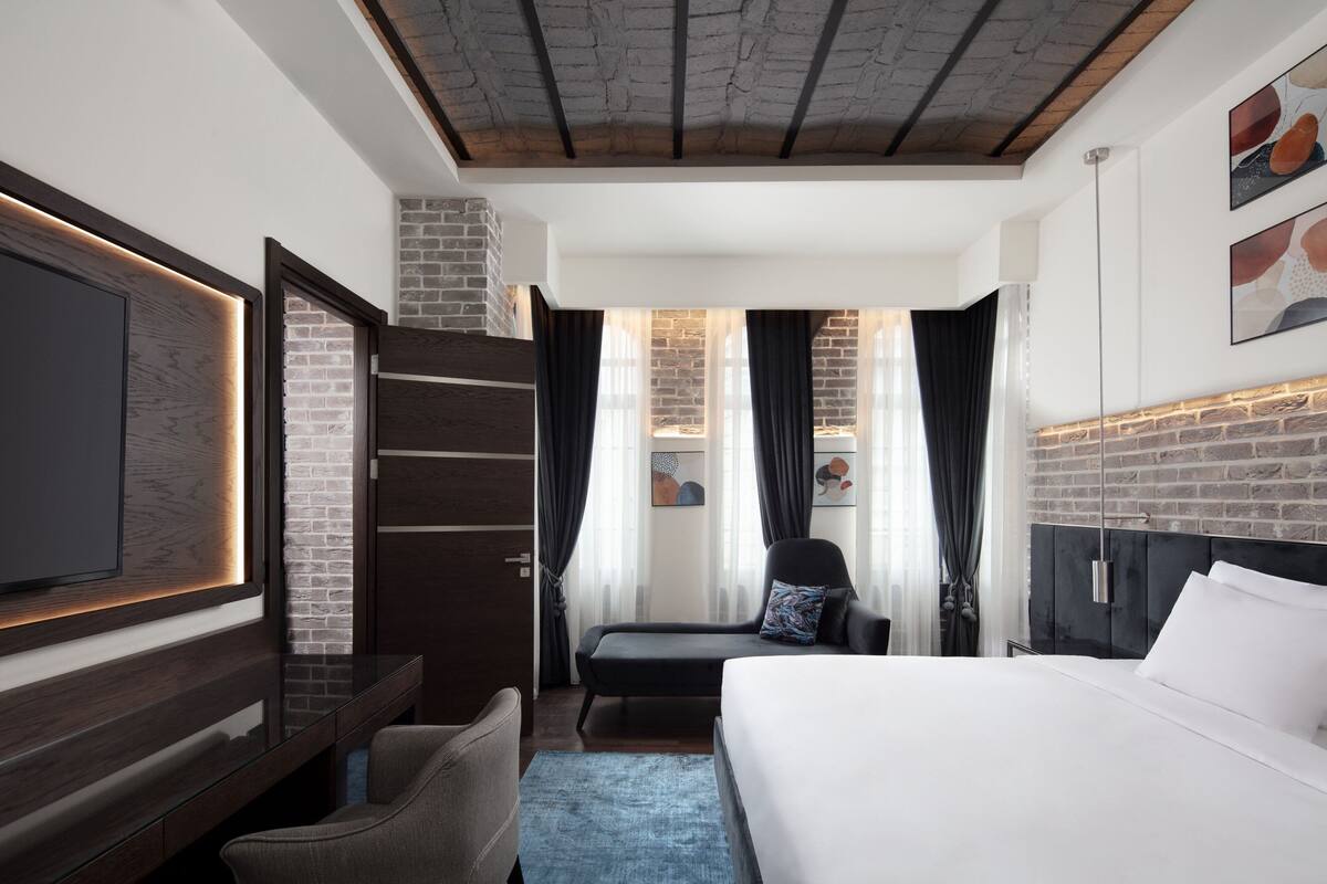 A modern hotel room with a large bed, a flat-screen TV, a seating area, and a brick accent wall.
