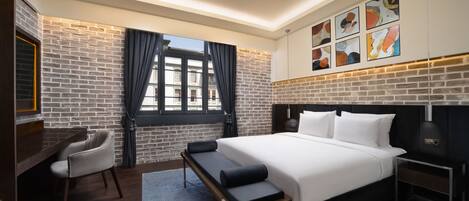 Habitación de hotel moderna con pared de ladrillo, una cama grande, un escritorio y una ventana con cortinas.