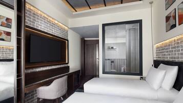 A modern hotel room with a brick accent wall, a flat-screen TV, a sofa, and a small seating area.