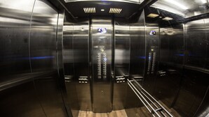 An elevator interior with metallic walls, a wooden floor, and control panels with illuminated buttons.
