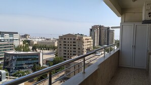 A balcony with a metal railing overlooking a cityscape with various buildings, including a tall residential building and a modern office building. - Bakuvi Tourist Apartment B056 (Baku)